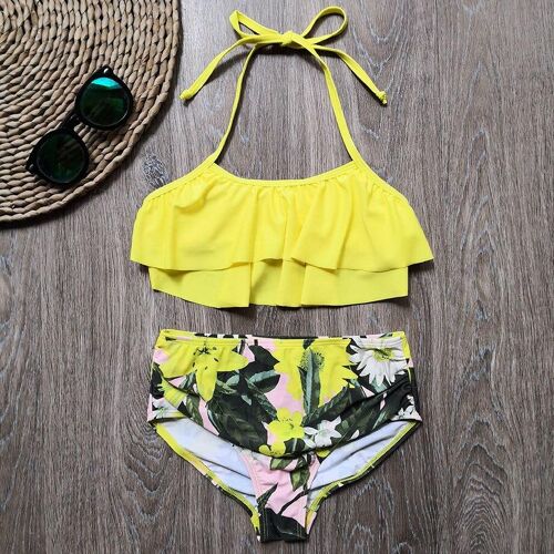Gelber Bikini mit Blumendesign auf Holzuntergrund, neben Sonnenbrille und runder Matte.