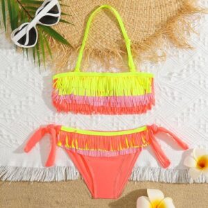 Bunter Bikini mit Fransen, Sonnenbrille und Blüten auf Sand und weißem Stoff.