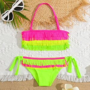 Neonfarbener Bikini mit Fransen und Sonnenbrille auf einem weißen Strandtuch.